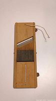 Top-down photo of vintage wooden mandoline slicer showing angled metal blade and slatted wood base with wire stabilization.
