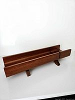 Side angle of teak bread slicer showing trough and feet