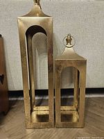 Both gold metal floor candle holders side by side showing size difference and design