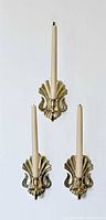 Three brass shell sconces displayed with candles inserted