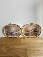 Pair of brass-framed oval pictures on tabletop