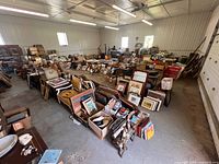 Wide view of warehouse interior showing tables and floor stacks of framed artwork, boxes of books and small items
