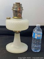 Front view of the full Aladdin milk glass oil lamp showing height and milk glass patterns next to water bottle for scale.