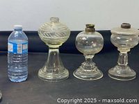 Photo showing three clear glass antique lamp bases side by side with a water bottle for scale