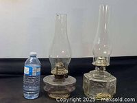 Two antique oil lamps side by side with a water bottle for scale.