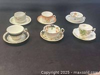 Six pairs of antique vintage teacups and matching saucers on a flat surface with visible floral patterns and gold detailing