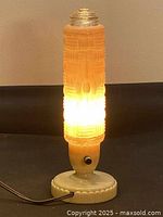 Art Deco torpedo-shaped pink glass lamp lit, showing warm glow through textured glass.