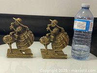 Front view of pair of brass bookend figurines with water bottle for scale.