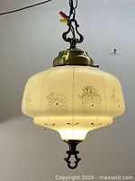 Full view of early pendant light fixture illuminated, showing cream etched glass shade with decorative patterns and metal fittings.
