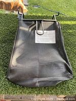Front view of new black mesh lawn bag with metal hooks, showing mounting hardware and attached label.