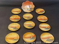 Full set with one large bowl and eleven matching saucers showing hand painted landscape scenes with windmills in warm orange and yellow lustreware glaze.