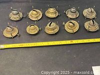 Top view of 10 vintage oil lamp burners of various metal finishes lined up with measuring tape showing about 16 inches total length.