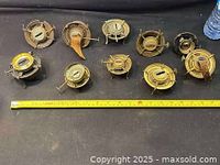 Set of 10 metal oil lamp burners arranged on a black surface showing front and top views, varying sizes and conditions, with visible wick adjusters and circular bases.