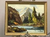 Framed oil on board landscape painting showing a river, trees, mountains, and sky.
