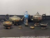 Overview of entire silver plate teapot set alongside water bottle for scale; shows two teapots, creamer, sugar bowl, two napkin rings, small pitcher