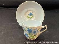Side view of the white porcelain teacup with hand painted blue flowers and green leaves, gold trim visible at rim.