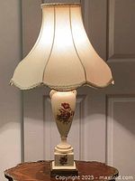 Front view of vintage porcelain lamp with floral painting on base topped with cream fabric lampshade
