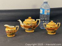 Tea set consisting of teapot, creamer, and sugar bowl shown beside a water bottle for scale