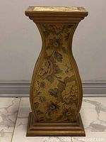 Front view showing curved floral patterned side panel of wooden pedestal with square top and base.