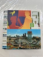 Front cover of the 2004 Canada postage stamp book showing colorful artwork including a silhouette of three figures and a carnival fairground scene with a roller coaster and city skyline.