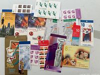Photo showing an assortment of Canada Postage Stamps mint, unused in booklets, sheets and loose stamps. Various themes visible such as Christmas, pets, international, university, and greeting cards.