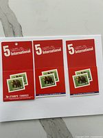 Three red Canada 5 International postage stamp booklets shown sealed and unopened with bear design stamps on front.