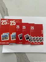 Five red booklets of Canadian postage stamps with face value 25 cents printed on the cover, laid on a white envelope on a marble surface.