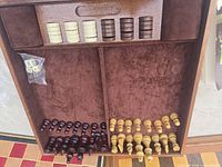 Interior of wooden game box showing chess pieces, checkers, and dice in felt compartments