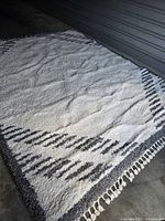 Top view of white and gray plush area rug showing pattern and tassels