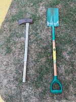 Photo showing a used ax with a metal head and white handle next to a garden shovel with a green metal blade, wooden shaft, and a green D-handle grip.