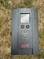 Top view of black APC Back-UPS RS 1500 unit showing LCD screen, control buttons, model and logo.