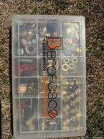 Closed view of a transparent plastic organizer box with the Brassco logo and website, showing various brass and metal plumbing fittings inside.