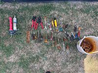 Wide view of assorted tools laid out on grass showing variety of hand tools and caulking supplies.