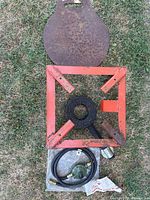 Top-down view of the entire kit showing hose with regulator, square red-orange metal frame with burner in center, and round rusted cast iron griddle plate.