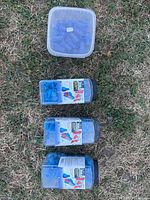 Top down view of 4 containers laid on grass, three labeled boxes and one unlabeled translucent container of blue plastic wire connectors