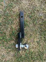 Top view of black metal trailer hitch ball mount lying on grass, showing the ball end and hitch receiver hole above