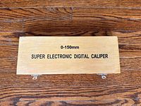 Closed wooden protective case with text '0-150mm SUPER ELECTRONIC DIGITAL CALIPER' printed on top.