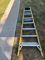 Full view of the Featherlite 8 ft step ladder laid flat on grass and sidewalk, showing entire ladder length and seven steps.