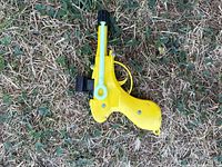 Yellow Greenlee CableCaster cable pulling tool laying on grass, showing side view with lever and spool mechanism.