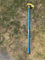 Full length photo of the conduit bender showing blue handle set on ground grass.
