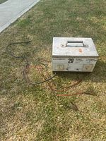 Full view of Motomaster battery charger with attached jumper cables positioned on grass.