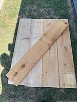 Five rough sawn lumber boards arranged on grass with one board placed diagonally on top showing wood knots and grain variations