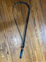 Full view of manual drain auger showing flexible black sheath, metal coiled cable, and curved end.