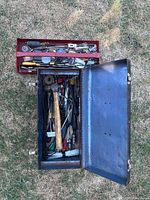 Open metal toolbox showing Estwing ball peen hammer, assorted hand tools, socket adapters, zip ties, and other small tools.
