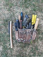 Photo of worn leather tool belt packed with screwdrivers, files, and wire brushes placed on grass.