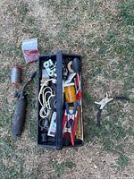 Top view of black plastic toolbox filled with assorted hand tools and accessories placed on grass