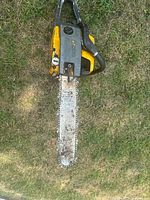 Top view of the yellow and black chainsaw placed on grass showing full length of cutting bar and chain with visible dirt and rust.