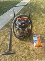 Full view of RIDGID wet/dry vacuum with hose attached, wide floor nozzle, and dust bags on grass.