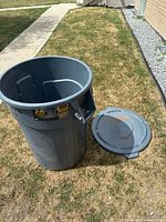 Rubbermaid BRUTE trash can with lid placed on grass outdoors, showing overall size and shape.