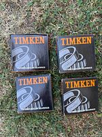 Four Timken branded black and orange boxes of tapered roller bearings arranged on grass. Each box has the model '386A' and states 'Tapered Roller Bearings' with a roller bearing graphic.